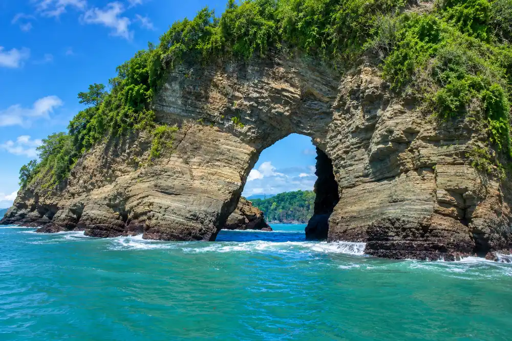 Natural rock arch covered in green vegetation rising from turquoise water on Costa Rica’s Pacific coast